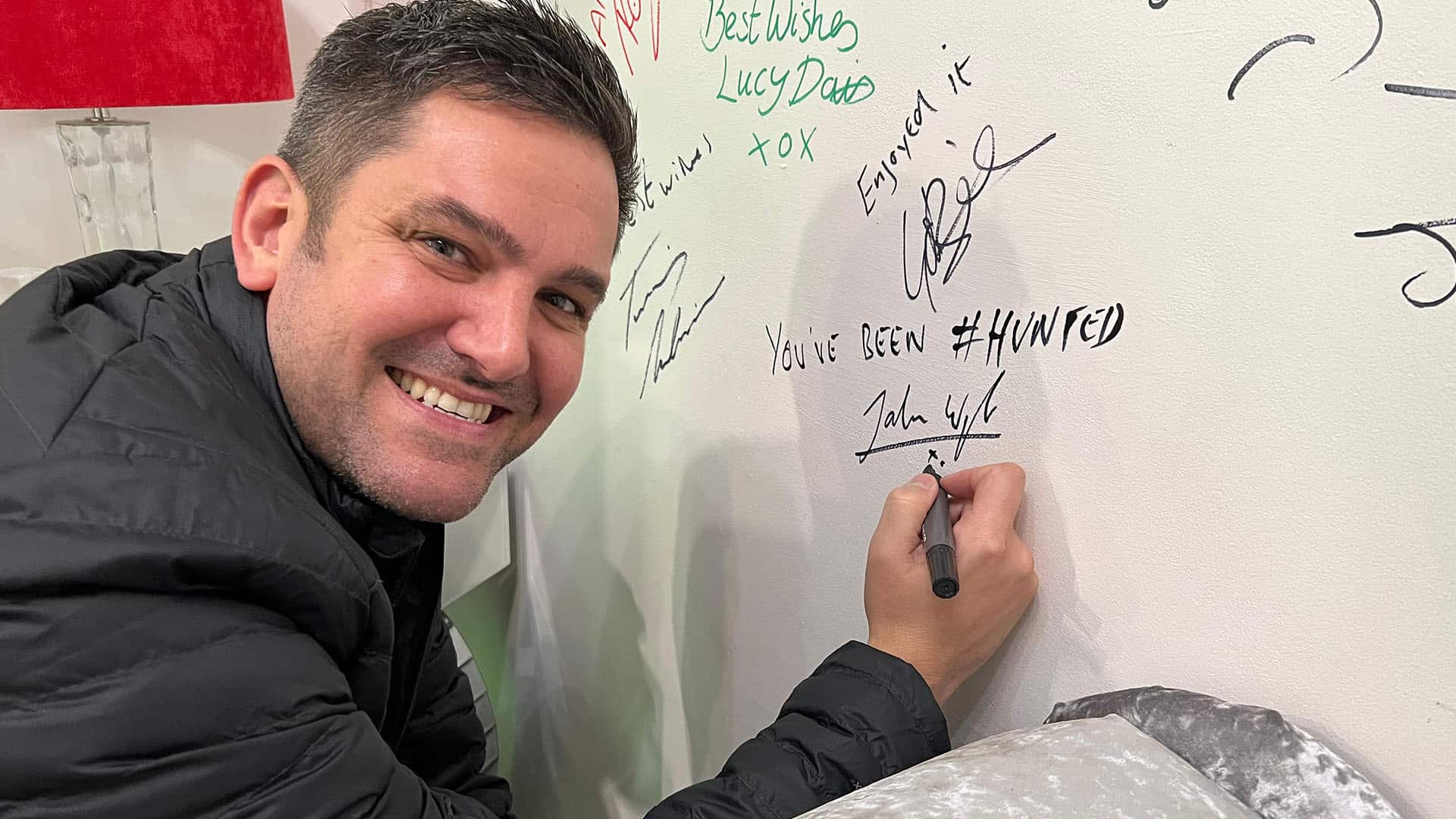 Smiling man signing a wall with marker